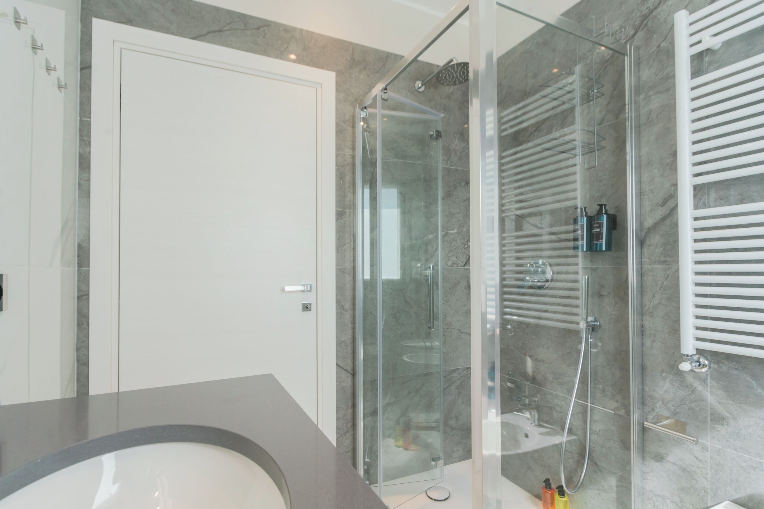 Ein modernes Badezimmer mit einer Duschkabine aus Glas, einer weißen Tür und einer Marmorwand.