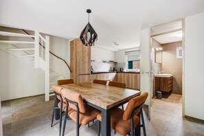 Een eetgedeelte met een houten tafel en stoelen, een trap en een keuken op de achtergrond.