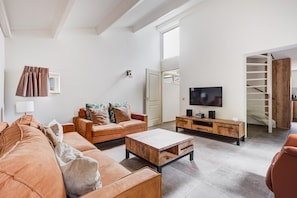 Een woonkamer met een bank, salontafel, televisie en een trap naar een vide.