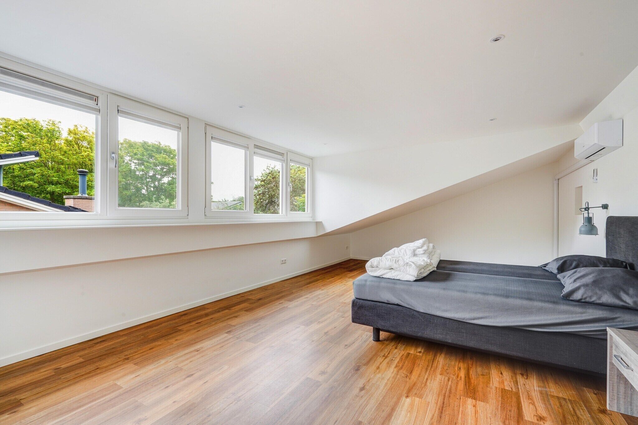 Une chambre avec un plafond de style industriel, de grandes fenêtres, un lit et un plancher en bois.