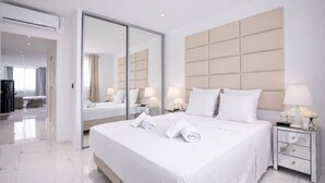 Moderni hotellihuone, jossa on suuri sänky, peili, yöpöytä lampun kanssa ja vaatekaappi.