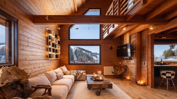 Ein Blockhaushaus-Interieur mit einer Couch, Kamin und großen Fenstern mit Blick auf eine verschneite Landschaft.