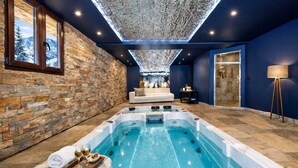 Ein Wellnessbereich mit Whirlpool, Steinwänden, einer Sitzecke und einem großen Fenster.