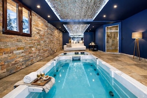 A spa area with a hot tub, stone walls, a sofa, and a large window.