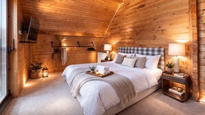 Ein Schlafzimmer mit Holzwänden, einem großen Bett, Nachttischlampen und einem an der Wand befestigten Fernseher.