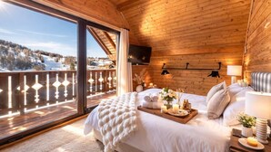 Ein Schlafzimmer einer Holzhütte mit großem Fenster, einem Bett mit Tablett mit Toilettenartikeln und einem an der Wand montierten Fernseher.