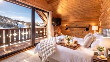 Un dormitorio de cabaña de madera con un ventanal grande, una cama con un atril de artículos de aseo y un televisor montado en la pared.