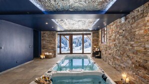 Ein Spa-Raum mit Whirlpool, Steinwänden und Blick auf verschneite Berge.