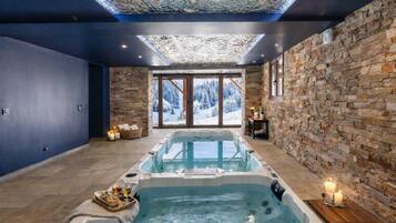 Un cuarto de spa con jacuzzi, paredes de piedra y vistas a montañas nevadas.