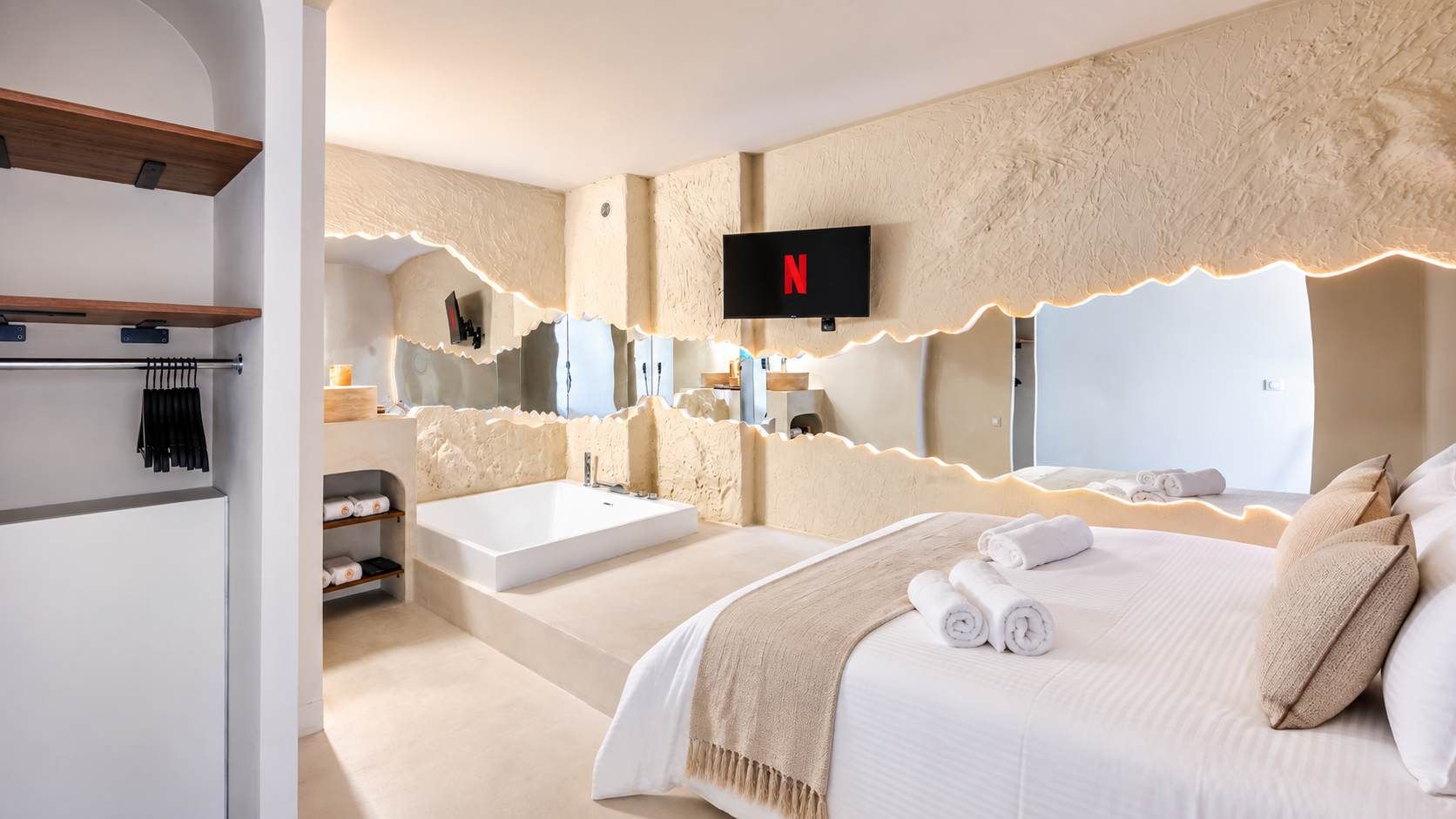 Een moderne hotelkamer met een groot bed, een aparte badkamer met een badkuip, een flatscreen televisie aan de muur en een grote spiegel die de kamer weerkaatst.