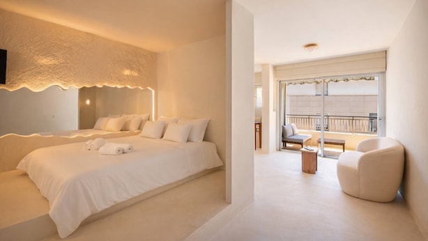 Una camera d'albergo moderna con un letto grande, una zona salotto con una sedia e un tavolino, e un balcone con ringhiera.