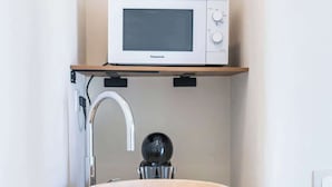Una cucina compatta con un lavandino rotondo, un rubinetto moderno, un forno a microonde e una lavastoviglie integrata.