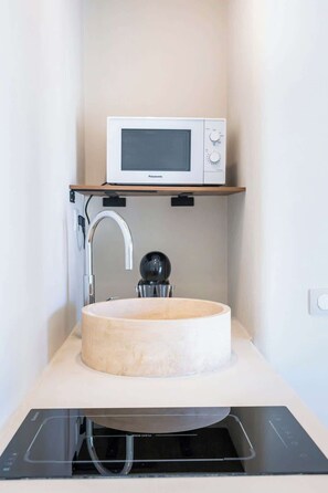 Eine kompakte Küche mit rundem Spülbecken, einem modernen Wasserhahn, einer Mikrowelle und einem eingebauten Geschirrspüler.