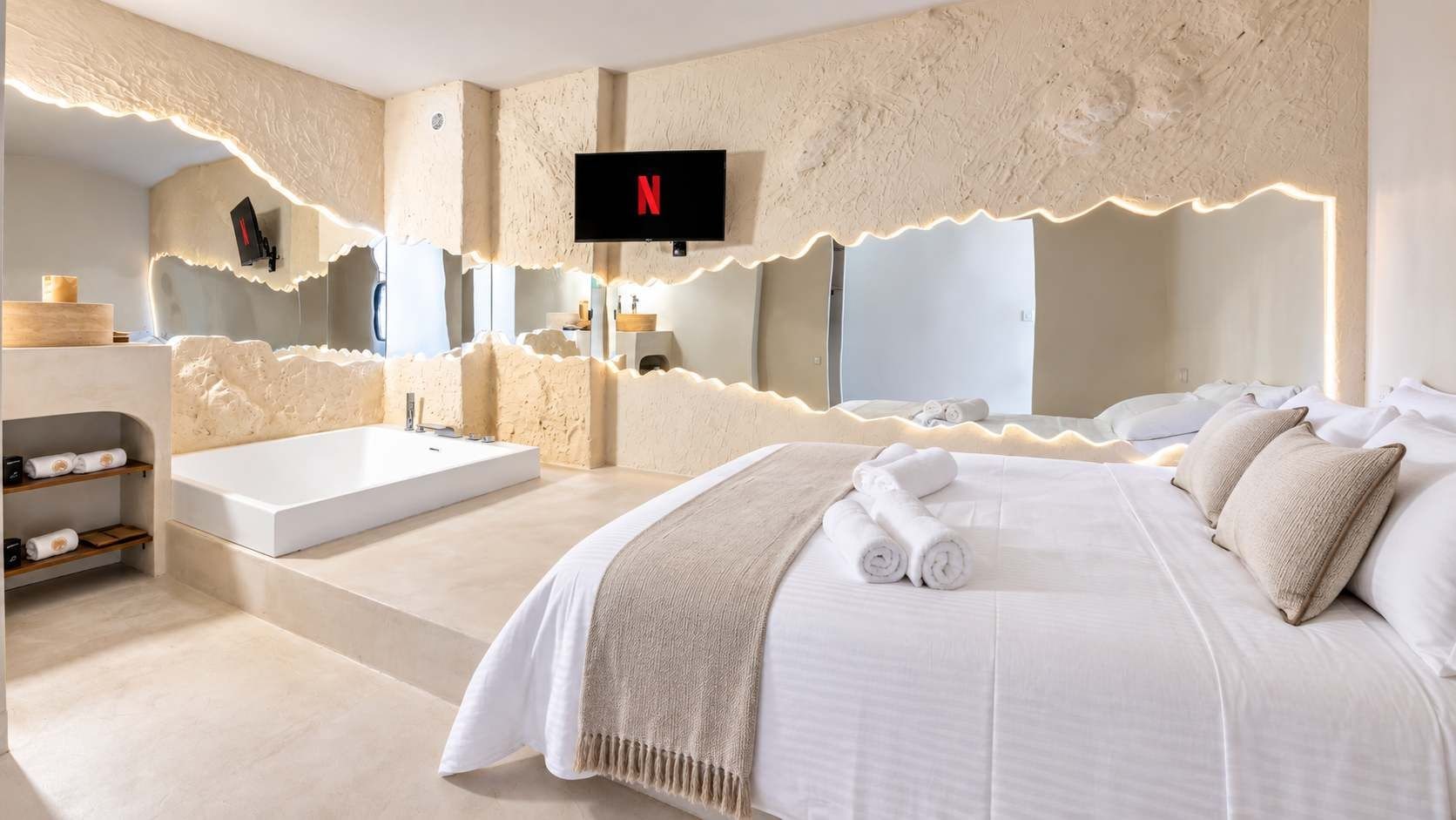 A modern bedroom with a large bed, a bathtub, and a TV mounted on the wall.