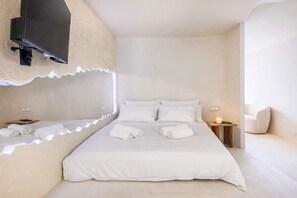 Un dormitorio minimalista con cama, mesitas de noche, televisor montado en la pared y una silla.