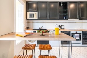 Eine moderne Küche mit dunklen Schränken, einer Holz Arbeitsplatte, einer eingebauten Mikrowelle, einer Kaffeemaschine und zwei Barhocker.