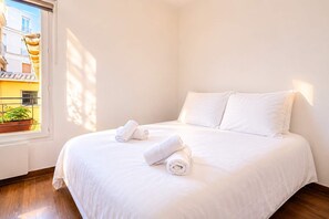 A neatly made bed with white linens and rolled towels, a window with a view of buildings, and a balcony with a railing and potted plants. - The Heart of Montmartre Triplex # 6 Guests - Wifi (Paris)