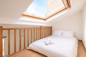 A bedroom with a skylight, wooden railing, and a bed with white bedding. - The Heart of Montmartre Triplex # 6 Guests - Wifi (Paris)