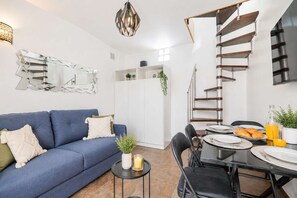A modern living room with a blue sofa, a dining table with chairs, a staircase, and a large mirror. - The Heart of Montmartre Triplex # 6 Guests - Wifi (Paris)