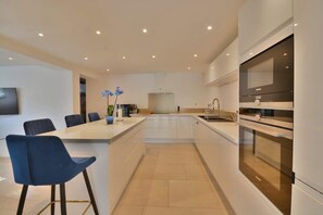 A modern kitchen with white cabinets, a central island with bar stools, a built-in oven, and a large window. - Villa Bella Vista # Pool - Luxury & Serenity (Le Cannet)