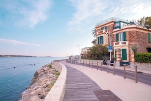 A coastal walkway with a stone building, a wooden boardwalk, and a view of the sea. - The Star of the Moure # Sea View - Beach - Port (Cannes)