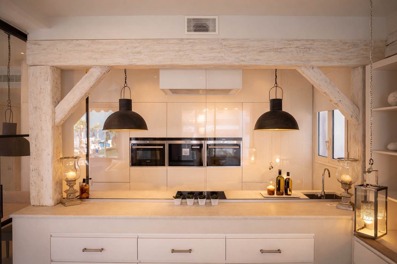 Een moderne keuken met een centraal eiland, dubbele ovens, hangende verlichting en een rustieke balkenplafond.