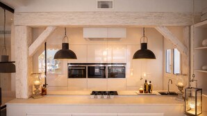 Una cocina moderna con una isla central, hornos dobles, iluminación colgante y un techo rústico.