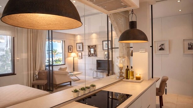 Habitación de hotel moderna con un ventanal grande, un sofá, zona de comedor y cocina con estufa integrada.