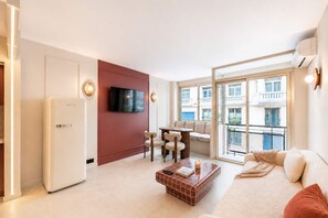 Un salon moderne doté d’un téléviseur à écran plat, d’un coin repas, d’un canapé et d’un balcon offrant une vue sur les bâtiments.