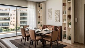 Une salle à manger moderne avec une table en verre, des chaises de couleur beige et une vue sur les immeubles à travers de grandes fenêtres.