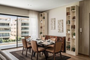 A modern dining room with a glass table, beige chairs, and a view of buildings through large windows. - Breeze @ Lakeview Res I Nesty Hospitality (New Cairo City)