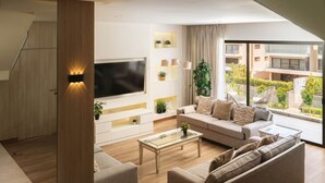 Un salon moderne doté d’un grand téléviseur à écran plat, d’un canapé, d’une table basse et offrant une vue sur un immeuble grâce à de grandes fenêtres.
