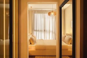 Ett modernt hotellrum med en stor säng, en hängande lampa och tunna, genomskinliga gardiner.