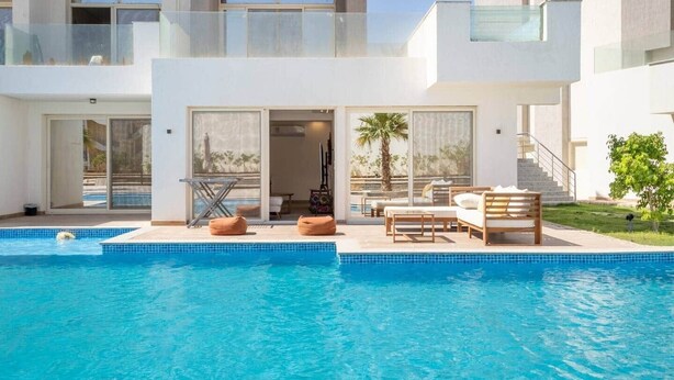Una casa moderna de dos pisos con piscina, mobiliario exterior y vistas del paisaje circundante.