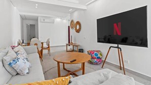 Una sala de estar moderna con un sofá, una mesa de centro, un televisor montado en la pared y una pequeña mesa con sillas.