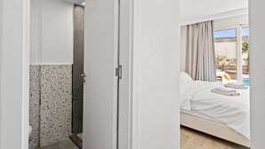 Habitación de hotel con cama, baño con ducha y vista a una piscina.