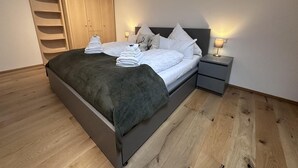A neatly made bed with white linens and a dark blanket, a wooden wardrobe, and a bedside table with a lamp. - "AllgäuLiebe", Oberstaufen (Oberstaufen)