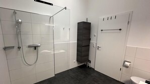 A modern bathroom with a glass shower enclosure, a dark floor, a white toilet, and a towel rack. - "AllgäuLiebe", Oberstaufen (Oberstaufen)