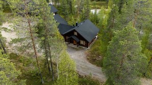 A cabin surrounded by dense forest, with a gravel driveway leading to the entrance.