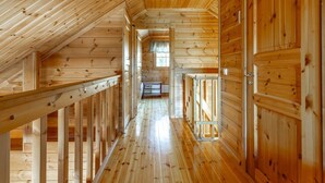 A wooden interior with a sloped ceiling, a central hallway, and wooden doors.