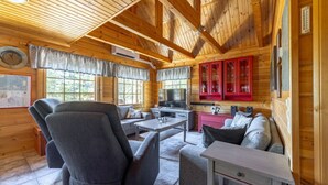 A cozy cabin interior with a wooden ceiling, a dining area, a sofa, and a kitchen with red cabinets.