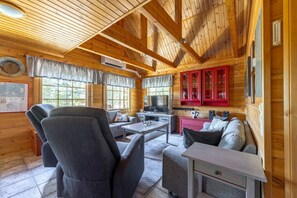 A cozy cabin interior with a wooden ceiling, a dining area, a sofa, and a kitchen with red cabinets.