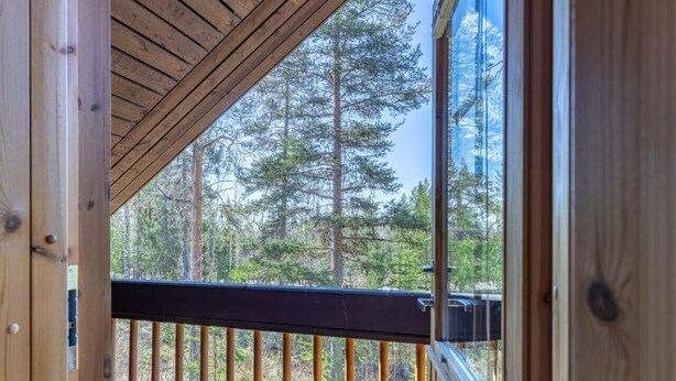 A wooden deck with a railing, a view of tall trees, and a clear sky.