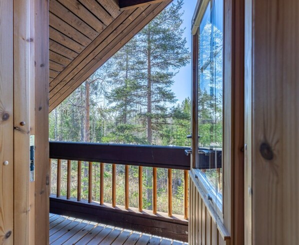 A wooden deck with a railing, a view of tall trees, and a clear sky.