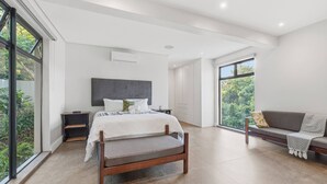 Ein modernes Schlafzimmer mit Bett, Bank und großen Fenstern.
