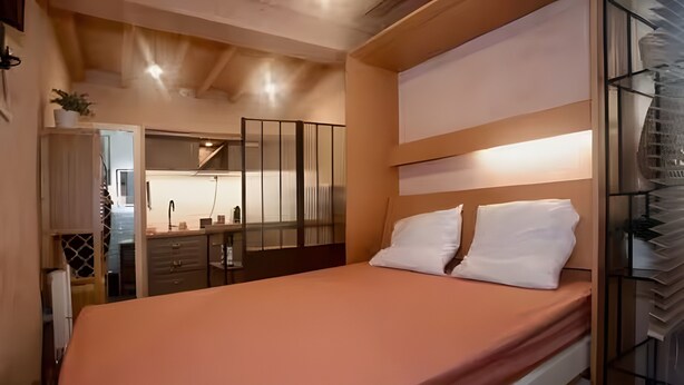 Une chambre à coucher avec un lit, des tables de chevet, un miroir et une vue sur la cuisine.