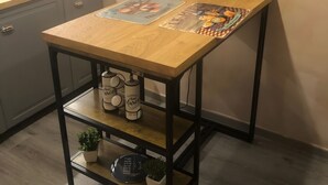 Une cuisine avec une table en bois, une machine à café et une petite plante posée sur une étagère en métal.