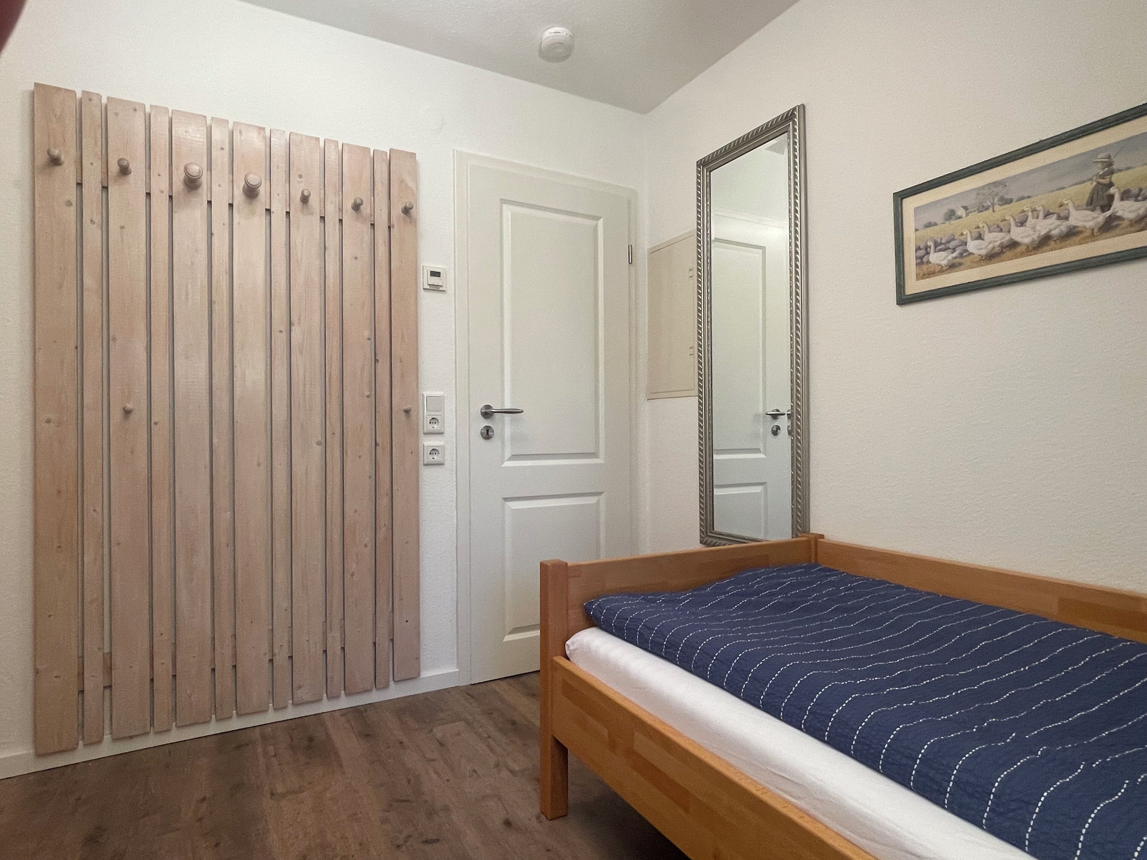 Ein Schlafzimmer mit einem hölzernen Bett, einer weißen Tür und einem Spiegel an der Wand.