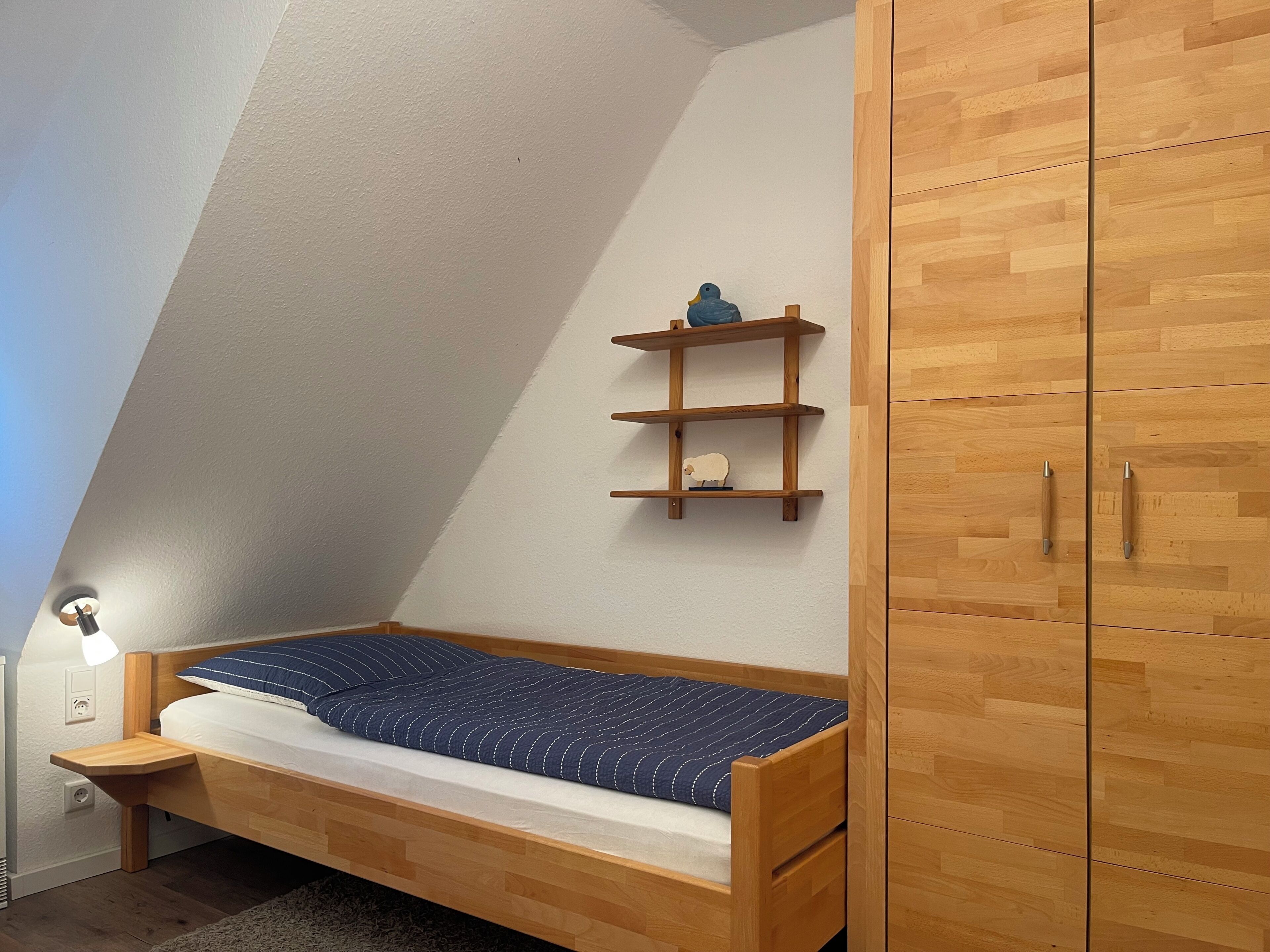 Una habitación pequeña con techo inclinado, una cama litera de madera, un armario de madera y un estante con adornos.