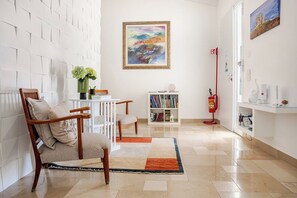 Un moderno salón con pared de ladrillo blanco, una silla de madera, una mesita con un florero, una estantería y un cuadro.